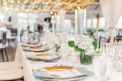 table set with white linens, white seat covers, blue hydrangea and tall glass pillars with candles.