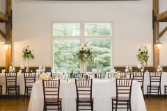 room with white wall with central window and white tables with tall white flower vases and wooden chiavari chairs