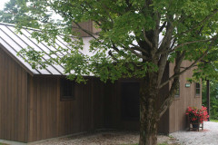 brown wooden cabin-like structure with metal roof and green tree.
