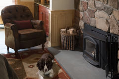 Dog sitting in front of leather chair in front of a stone fire place next to pile of wood at Mountain Top Inn & Resort in Chittenden, VT