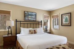 photograph of cloud nine guest home bedroom. bed is featured in the middle of the room, with a nightstand on either side with a lamp on top. windows are on each side of the bed as well. there is a framed painting above the bed.