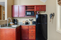 photograph of guest home, cloud nine. photograph is of kitchen. cabinets are red, and the kitchen features a small sink, coffee maker, and other essentials. fridge is black and is on the right side.
