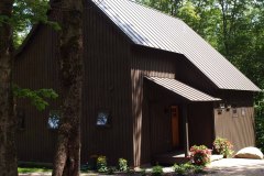 exterior of brown wooden house with steep metal roof in summer.