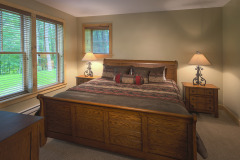 sleigh style brown wooden bed beside windows with decorative pillows and bedspread.
