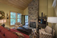 Living room with couch and comfy chairs facing fireplace with tall stone chimney.