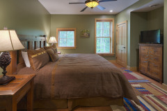 bedroom with brown coverlet on bed, wooden dresser, window and multi colored rug.