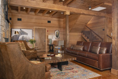 Wooden interior of Foley Farmhouse, showing open-concept living room with leather sofa, wooden table, high beam ceilings and staircase.