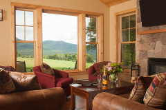 Mountain Top Resort Grand Vista Guest House living room with fabric arm chairs and large windows showing view out to green meadow and hills.