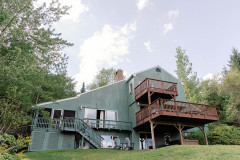 exterior of green 3-story wood sided building in summer with large 2 story deck.
