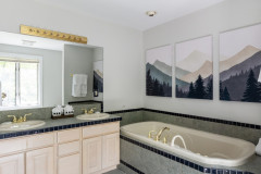 master bathroom featuring a tub, two sink vanity, and mountain based artwork on wall.
