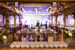 Mountain Top Resort reception hall with wooden beams and farmhouse tables throughout with table in front showing name cards for guests.  purple lights and blurry figures in background.