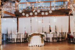 Mountain Top Resort reception hall in barn with wooden beams. Decorated with round tables with white linens and white drapery, white snowflake ornaments hanging from beams.
