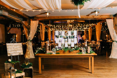 Mountain Top Resort reception hall with wooden beams and farmhouse tables  with wedding guests sitting in them.  lights and drapery hanging from beam and welcome table set-up in front.