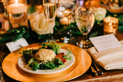 Table set with gold charger under white plate.  Salad with breaded cheese ball on top, white napkins, glasses with water and champagne.