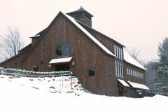 large wooden barn with big windows and a steeple surrounded by snow.