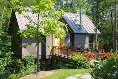 Tiny house tee house, brown wood with brown metal roof and elevated bridge walkway to door.