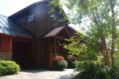 Front of house with wood siding, peaked roof and pent roof over entranceway. summer trees.