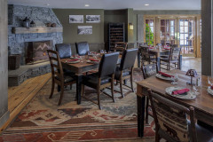 Dining room with leather chairs at wood tables, multi-colored rug and stone fireplace.
