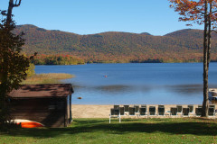 lake surrounded by autumn trees on mountains with beach and beach chairs in foreground.