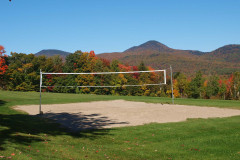 sand volleyball court against backdrop of foliage covered mountains and blue sky.