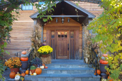 front entrance of wooden building with pent roof, stone steps and decorated with pumpkins and mumms.
