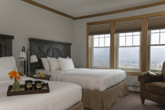 Bedroom with 2 queen beds, 3 windows along wall with view out to snowy trees.