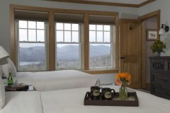 Bedroom with 2 beds covered in white sheets, breakfast tray with mugs and flowers and windows with view out to snowy hills.