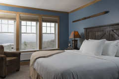 Bedroom with blue walls, king bed with large dark wood headboard and windows with view out to woods.