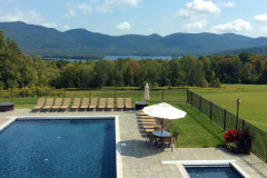 inground pool and hot tub with tan lounge chairs on patio and mountains and trees in background.