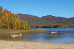 lake with 2 canoes and foliage covered mountains.