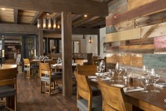 restaurant dining room with wooden chairs and tables set with glasses and silverware, post and beam construction and multi-colored barn board wall.
