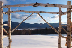 A manmade birch arbor with a view toward the snow and mountains with an expansive blue sky.