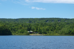 view across blue water to sandy beach and barely visible pavilion amidst green trees.