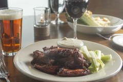 chicken wing dish accompanied by a salad, pint of amber beer and glass of wine on wood table.