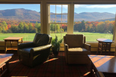 view from inside room with comfy leather chairs against window. outside window is view of brightly colored mountains covered in foliage.