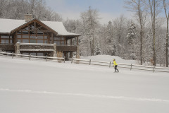 Mountain Top Resort cross country skier with yellow jacket passing The Jewel at Meadow's Edge Guest House in snowy field near trees