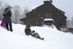 Two people sledding on snowy hills in front of wooden barn at Mountain Top Inn & Resort in Chittenden, VT