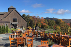 Outdoor wooden tables and chairs with floral centerpieces in front of wooden barn on stone patio at Mountain Top Inn & Resort in Chittenden, VT