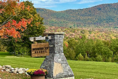 Stone pillar with sign reading mountain top resort in foreground, foliage trees and mountains in background.