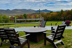 portable firepit surrounded by adirondack chairs with foliage covered mountains in background.