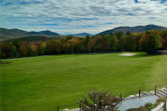 early fall view across lawn to foliage covered mountains with white fluffy clouds in blue sky.