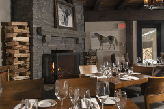dining room with wooden tables and wood stacked by grey stone fireplace.