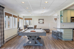 living area in sunrise guest home in the basement featuring a grey wooden pool table, small dining table,  and small view of the kitchen space.