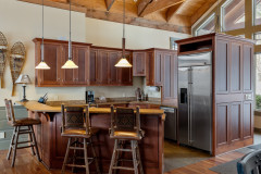 Mountain Top Resort Jewel Guest Home kitchen. Featuring three barstools on front side of island, with kitchen showing a large stainless steel fridge on the right side, with dark wooden cabinets creating an alcove of space. 