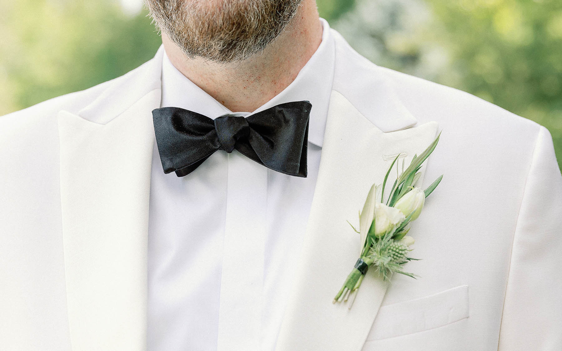 close-up of man in white suit with black bowtie and white and green boutonniere.