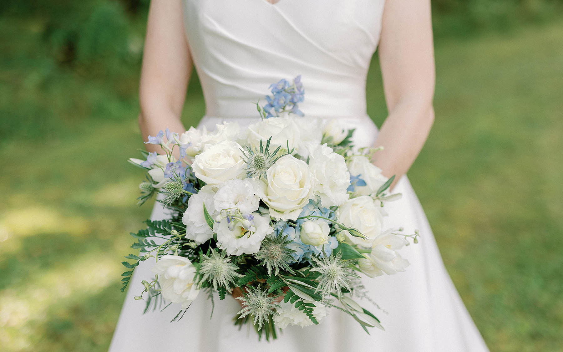 bride in white dress holding bouquet of white, blue and green flowers.