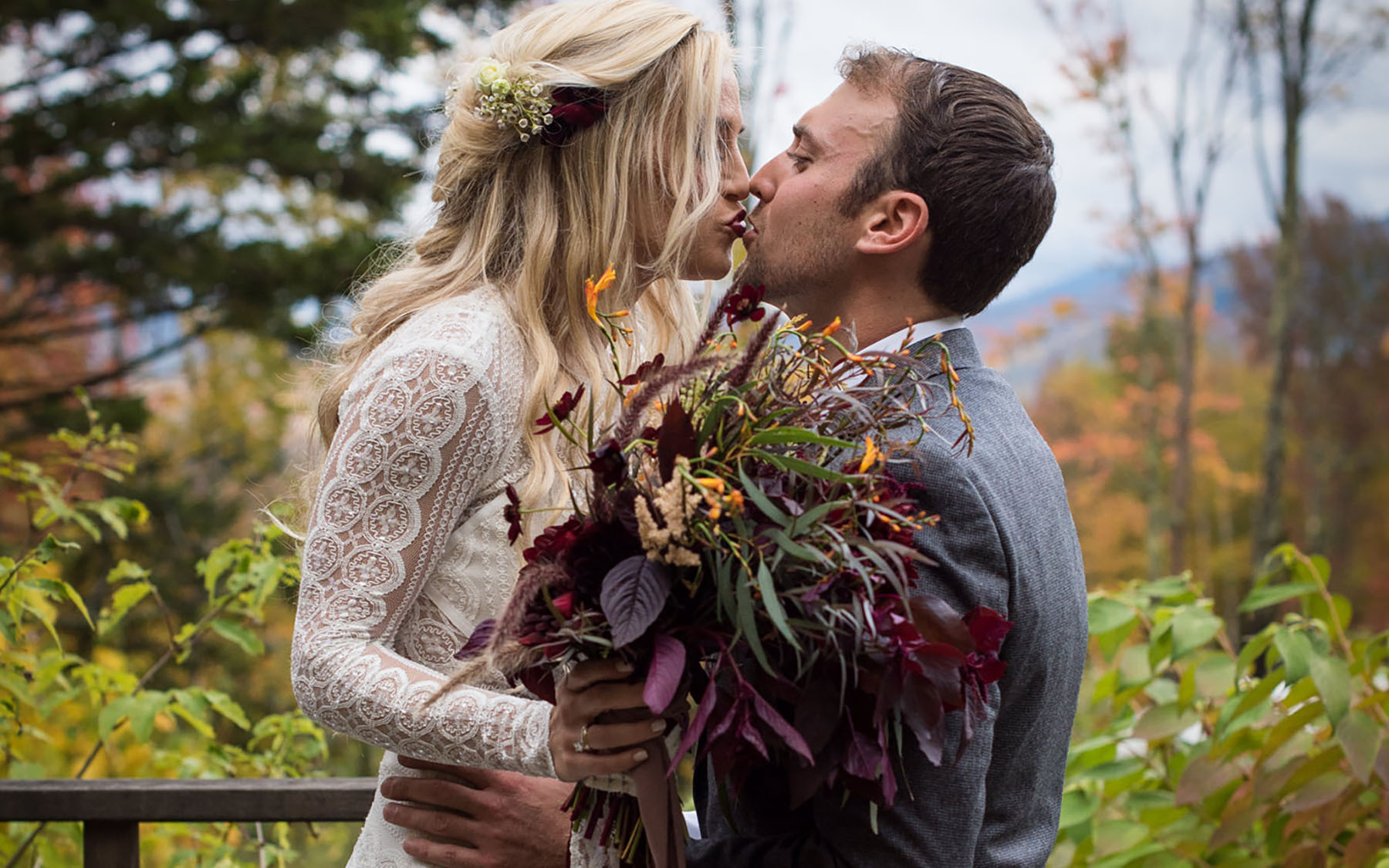 a bride and groom in traditional dress, holding wild fall flowers, kissing.