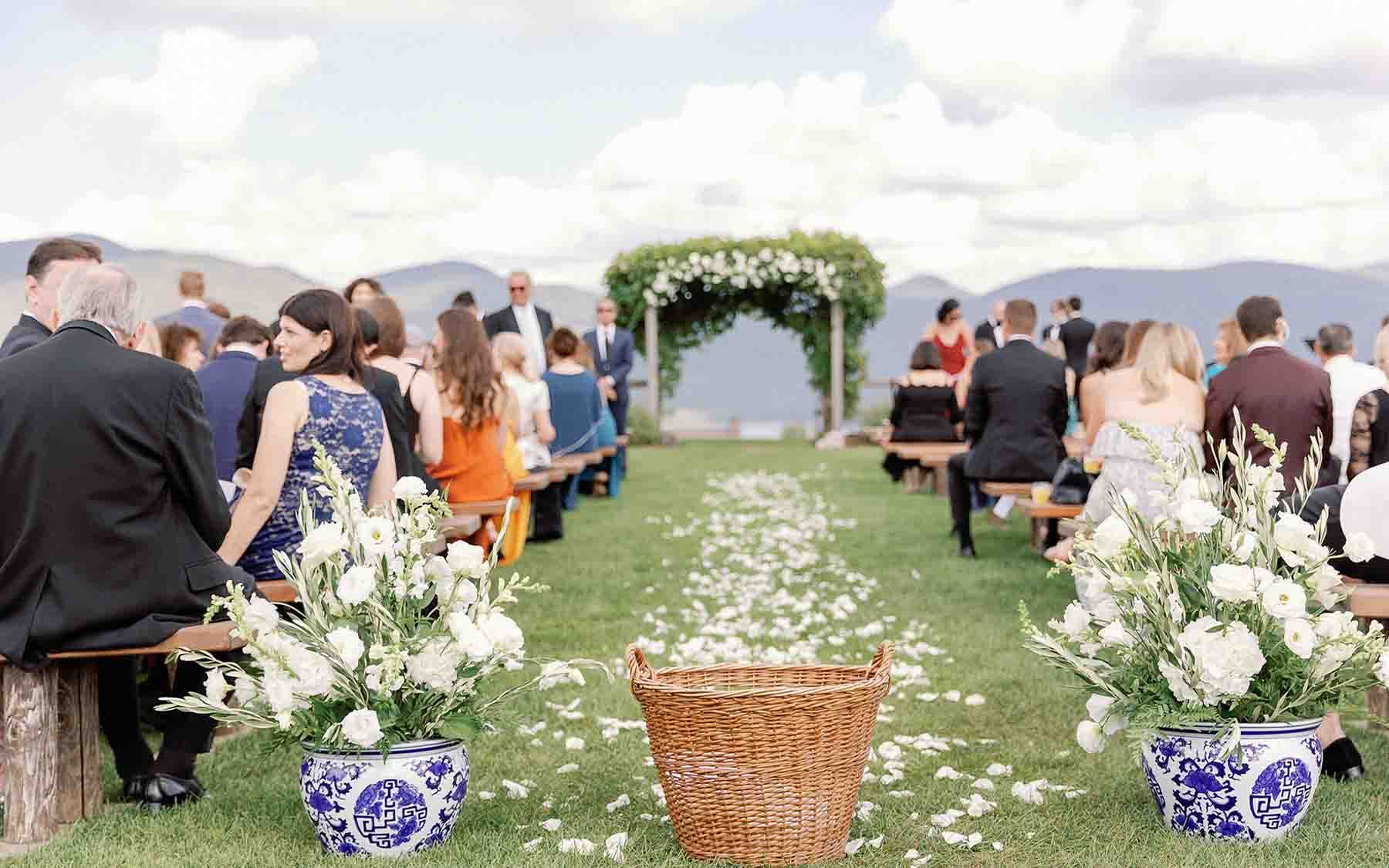 outdoor wedding ceremony with white flower petals strewn along aisle and guests sitting on benches.