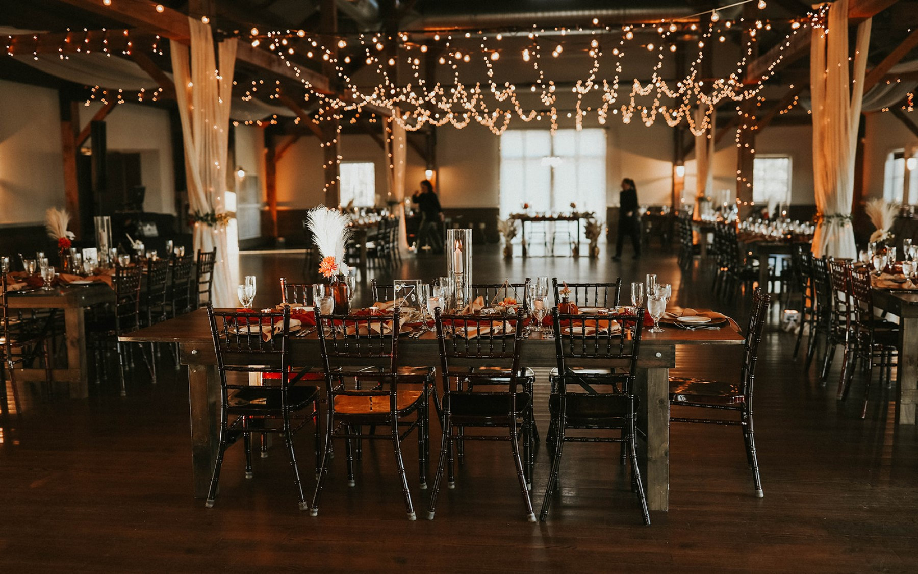 event barn setup with farmhouse tables, chairs, and string lighting towards the ceiling with drapery.