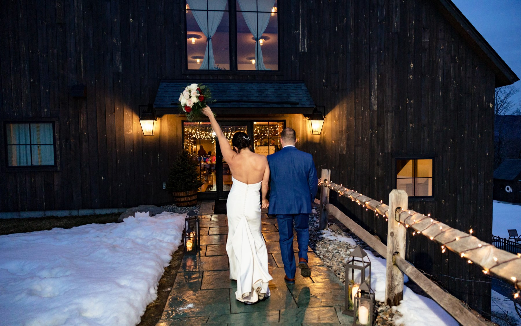 bride and groom in winter walking to dark wooden event barn on path